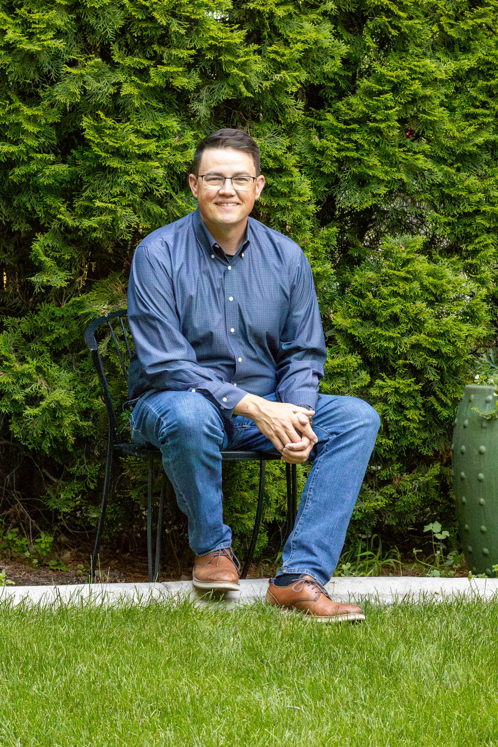 Seated portrait of Chris Corry on a chair by some bushes