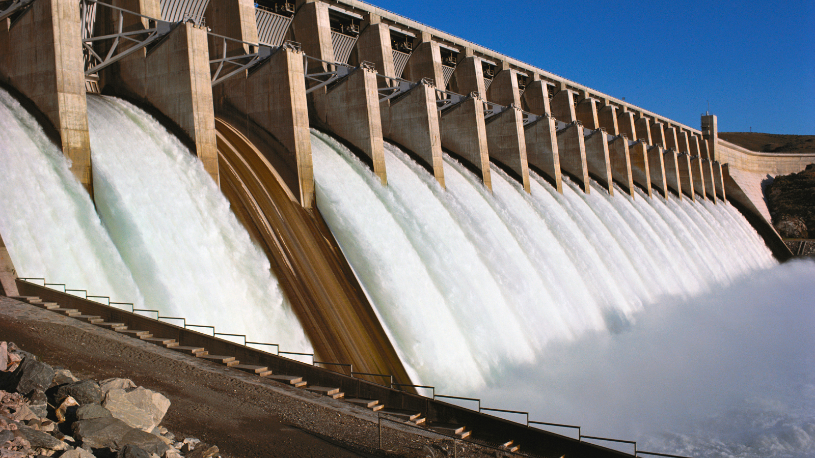 A large hydroelectric dam with water cascading over its spillway under blue Pacific Northwest sky