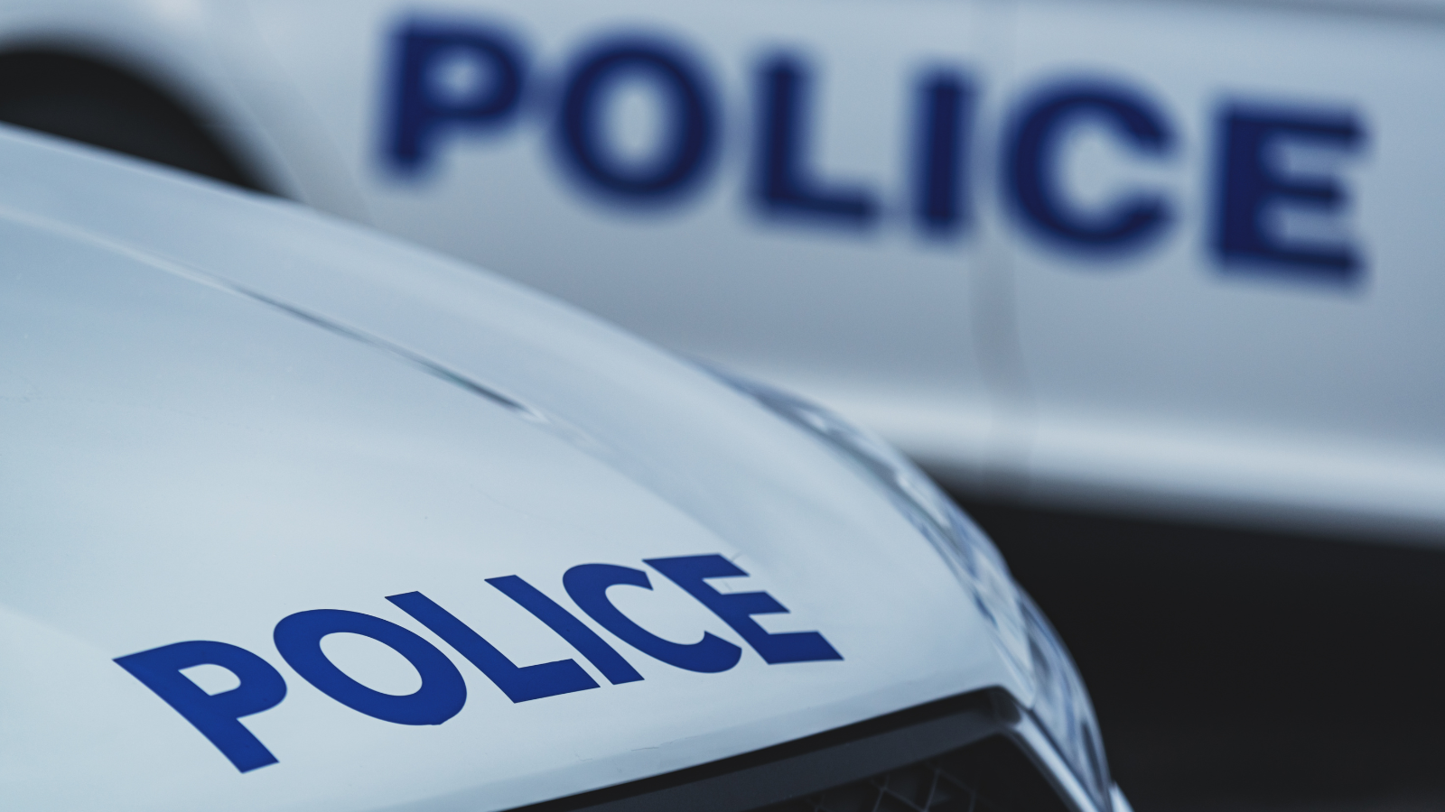 Close-up of two parked police vehicles, the word POLICE in dark blue lettering visible across their hoods